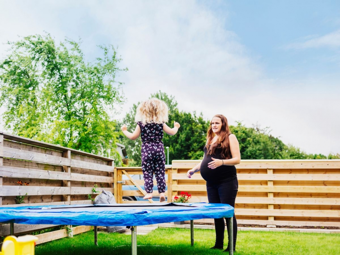 A pregnant woman watching over her child as she plays on a trampoline.jpg